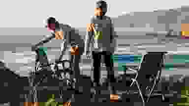 Two travelers setting their beach chairs up beside a large body of water.