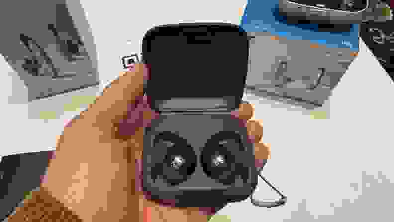 A hand holds a pair of Sennheiser Momentum Sport in their gray carrying case.