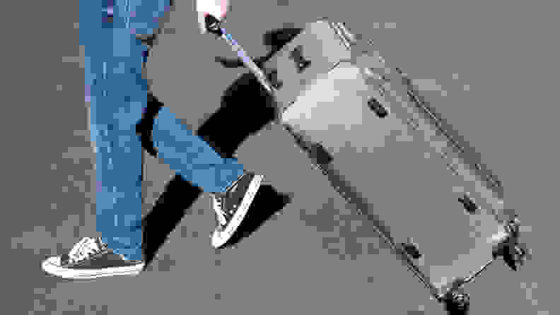 A wheeled suitcase is pulled across a paved street