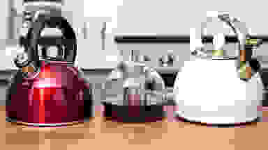 Three tea kettles, including the Cuisinart Aura, the Hiware glass kettle and the Susteas teapot, sit on a kitchen counter.