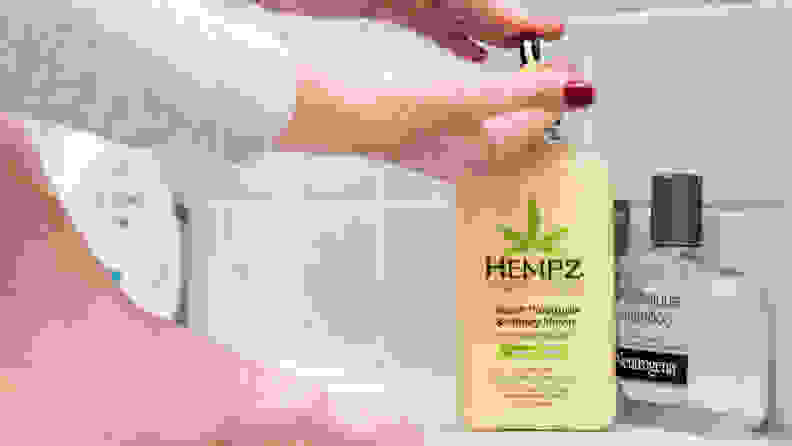 A person's hand pumping a bottle of Hempz Moisturizing Skin body lotion.