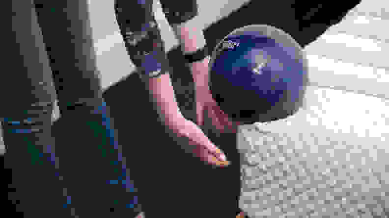 Hands catch a bowling ball that's about to roll off the edge of the mattress.