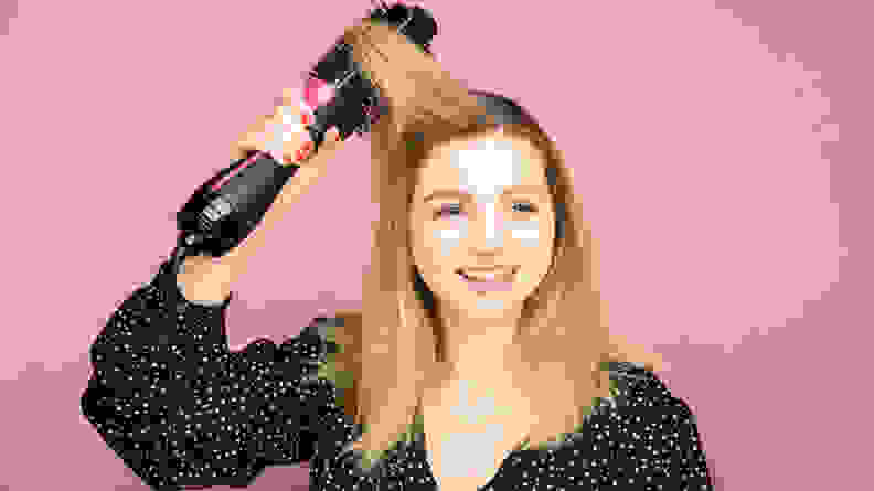 A woman running a hair dryer brush through her blond hair.