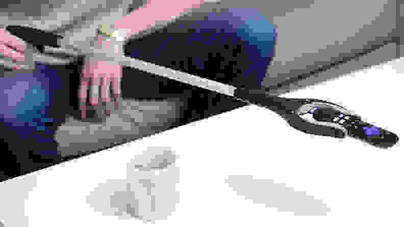 A person uses a reacher grabber to pick up a TV remote