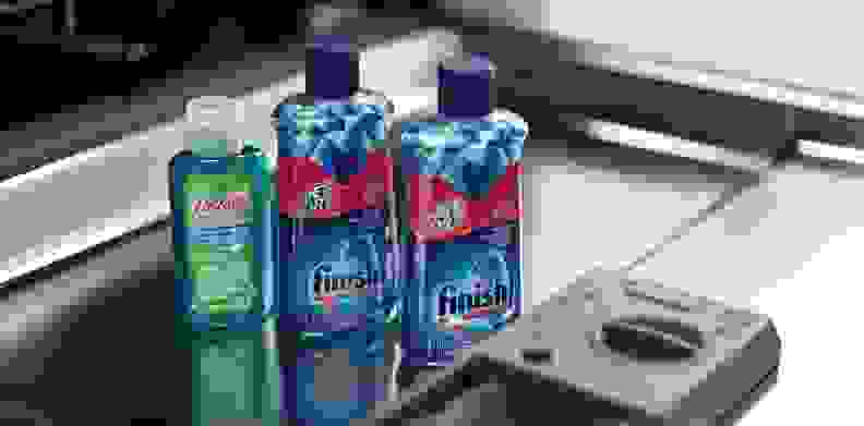Three bottles of rinse aid sit on the open door of a dishwasher.