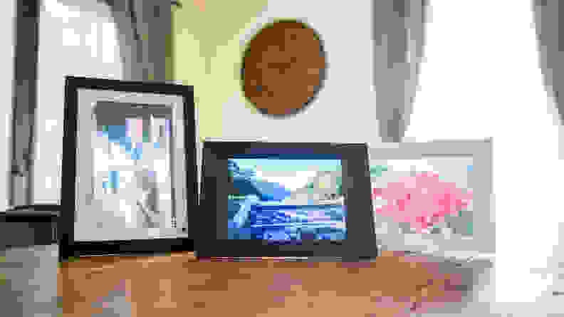 Three digital picture frames displaying colorful florals sit on a wooden table.