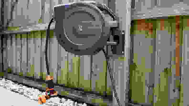 The Giraffe Tools Retractable Garden Hose Reel hangs on a fence in a backyard