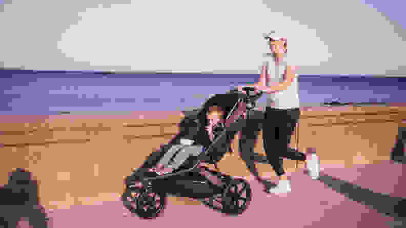 A woman jogging along a sea wall pushing a child in a jogging stroller.