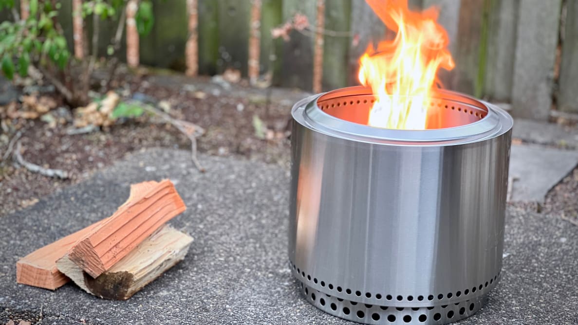 Solo Stove Bonfire 2.0 with open flame outdoors next to firewood.