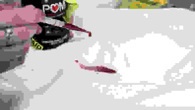 a pipette filled with red pomegranate juice drops liquid onto a mattress protector