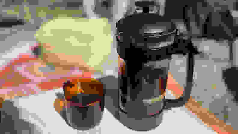 An Espro P3 French press with black plastic holder is pictured next to a brown-tainted glass mug on a table.
