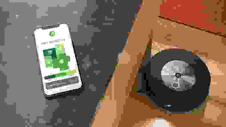 A smartphone on a gray countertop above a black and gold robot vacuum