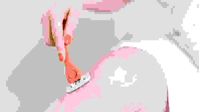 The author using the coral colored Billie razor to shave around her knee while sitting at the edge of a tub.