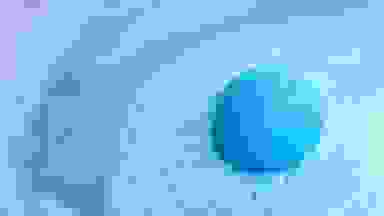 A blue bath bomb starts to foam turning the water around it different shades of blue.