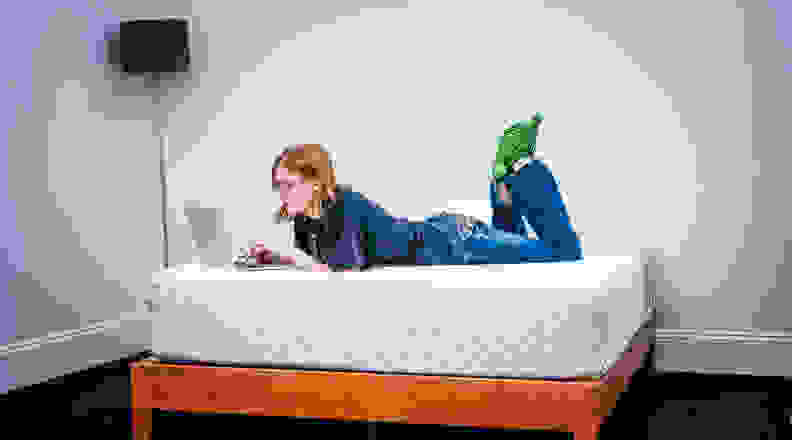 The Leesa Hybrid mattress sits in a room with a woman on it.