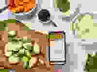 A countertop with healthy ingredients chopped, with a hand holding a phone that showcases a recipe