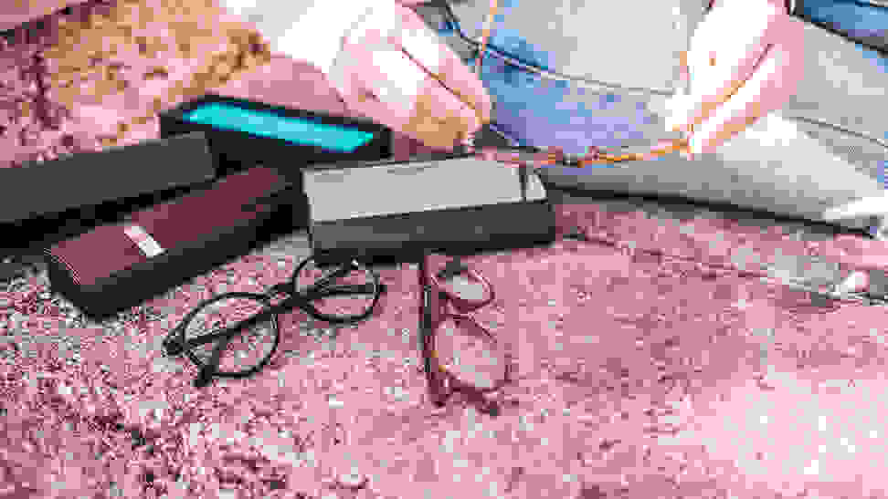 Two pairs of glasses and their boxes are spread out on a sidewalk while a woman holds a third pair.