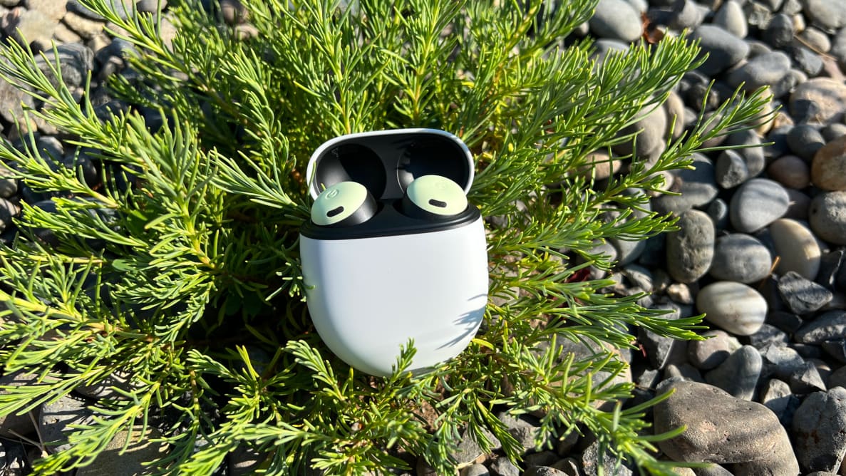 A pair of mint green Pixel Buds Pro lying on a plant in the center of some rocks.