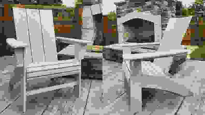 A side by side of the Polywood Modern Curveback Adirondack Chair sitting in front of an outdoor fire place