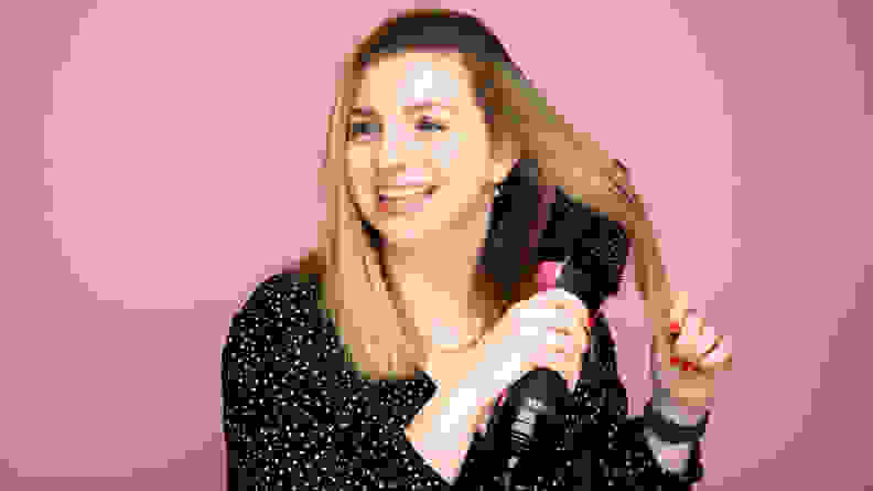 A woman brushing a hair dryer brush through her blond hair.