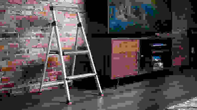 A step stool stands by a TV in front of a brick wall