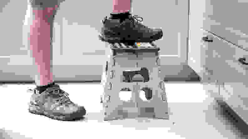 A person wearing sneakers steps on a low plastic stool
