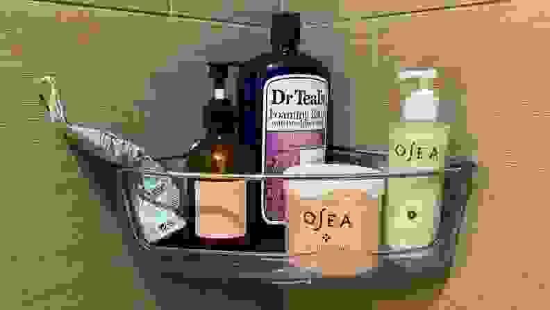 A corner shower caddy hangs in a tiled bathroom and is full of soap bottles