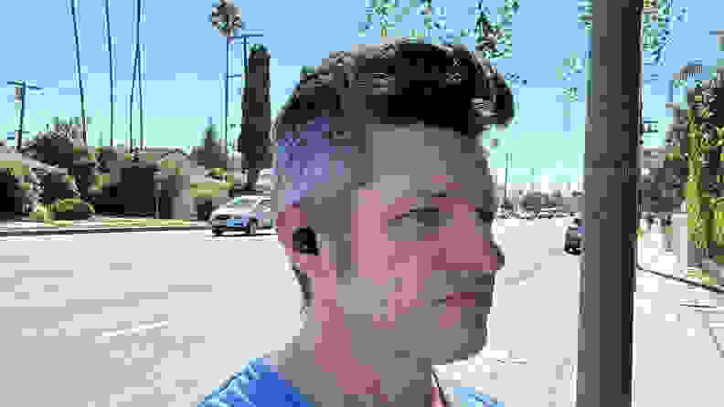 A man wearing the Sony WF-1000XM5 earbuds outside with car going by.