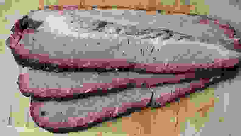 Three slices of smoked brisket on wooden surface.