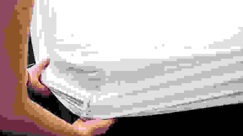 hands pull the Tuft & Needle mattress protector over the corner of a bed