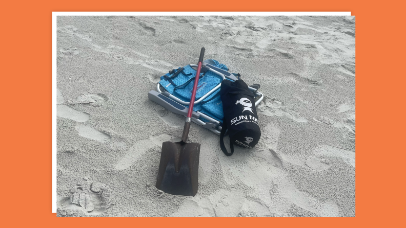 Tent, shovel and beach chair sit together on sandy beach.