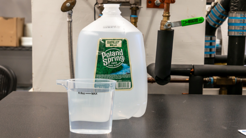 A jug of distilled water next to a measuring cup sitting on a table.