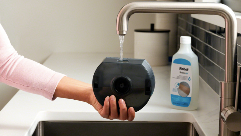 Someone pours water into a robot mop with a bottle of cleaning fluid on the counter