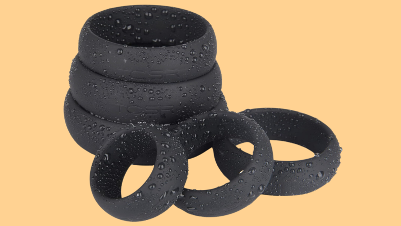 A stack of three silicone rings behind a row of three more silicone rings that are covered in water beads on an orange background.