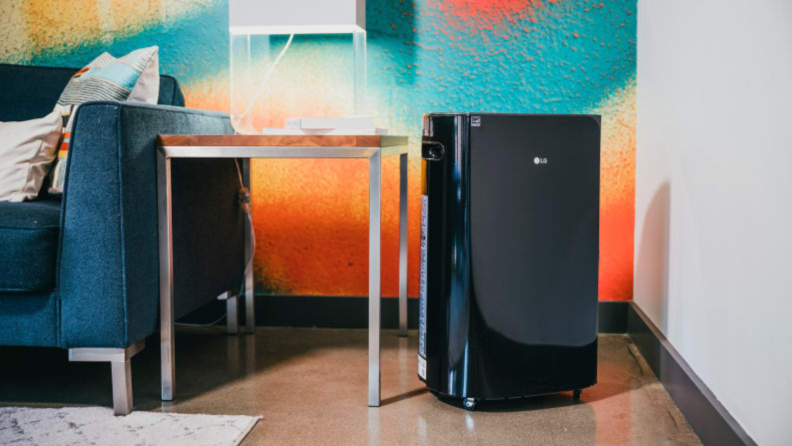 An LG dehumidifier sits next to a table in a room with a colorful wall