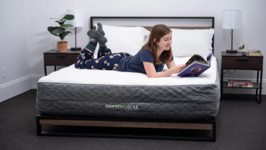 A woman wearing pajamas reads a book while lounging on a mattress.