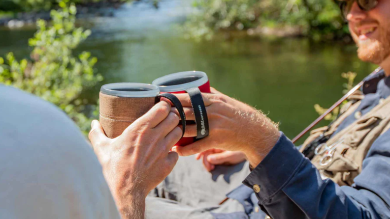 Two white men push coffee mugs together
