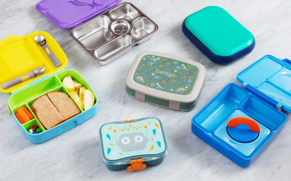A variety of brightly colored lunch boxes sit open and closed on a marble counter.