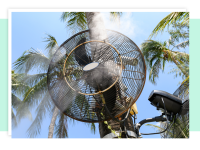 Circulating misting fan mounted onto post in front of palm trees outdoors.