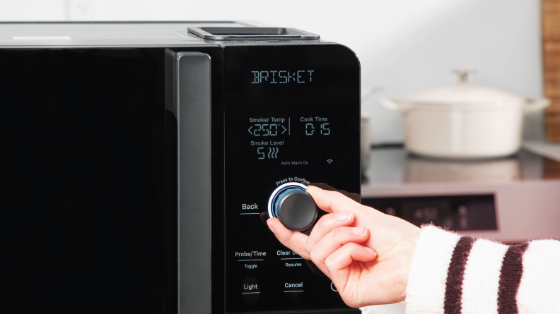A hand adjusting the dial on the smoker control panel