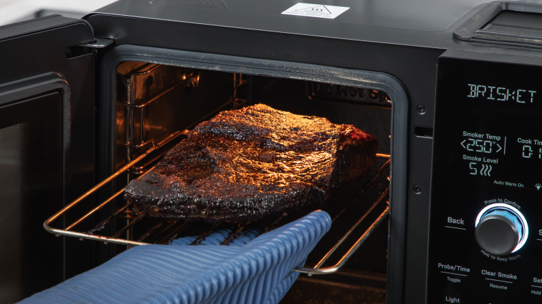Hand with oven mitt pulling a smoked brisket out of the GE indoor smoker