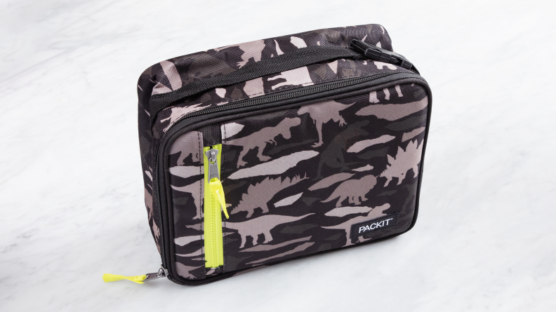 The PackIt Freezable Classic Lunch Box in dinosaur camo pattern on a marble counter.