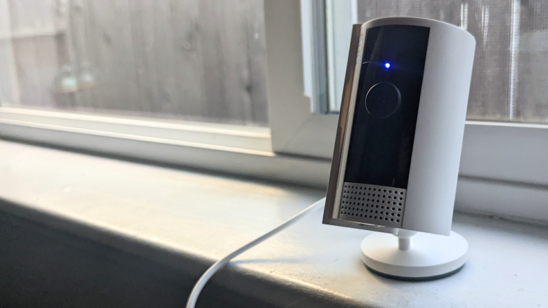 The second-gen Ring Indoor Cam with its shutter open sitting on a window sill with the blue light for recording enabled