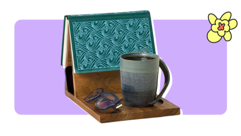 A hardcover book mounted on a wooden bookstand with a mug and a pair of reading glasses in front of purple background with a yellow cartoon flower in the corner.