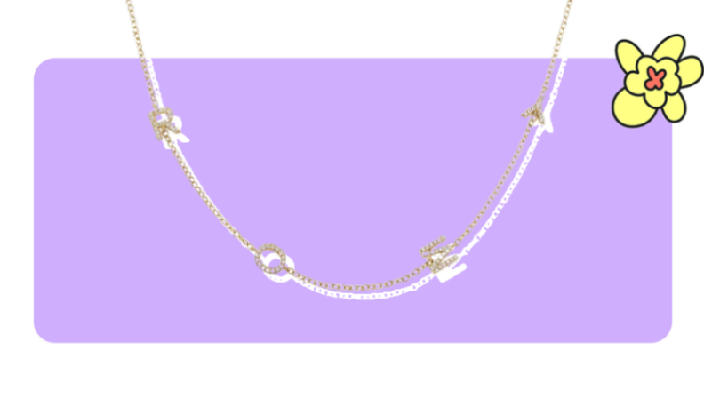 A gold pendant necklace with diamond-crusted letters in front of purple background with a yellow cartoon flower in the corner.