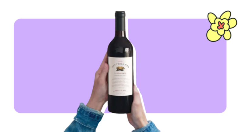 Two hands holding a bottle of a bottle of red wine in front of purple background with a yellow flower in the corner.