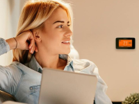 A woman sits down with a Sensi smart thermostat pictured on the wall behind her.