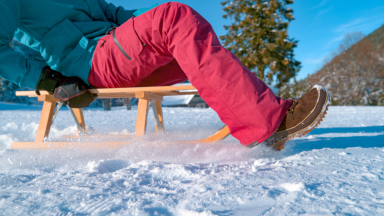 A model wearing snow pants glides across a frozen lake on a sled.