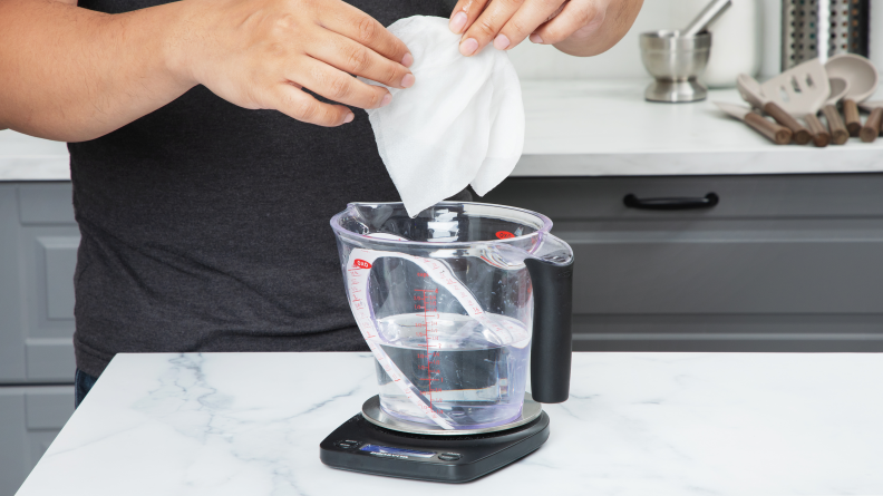 A person dipping a paper towel into a pitcher of water.